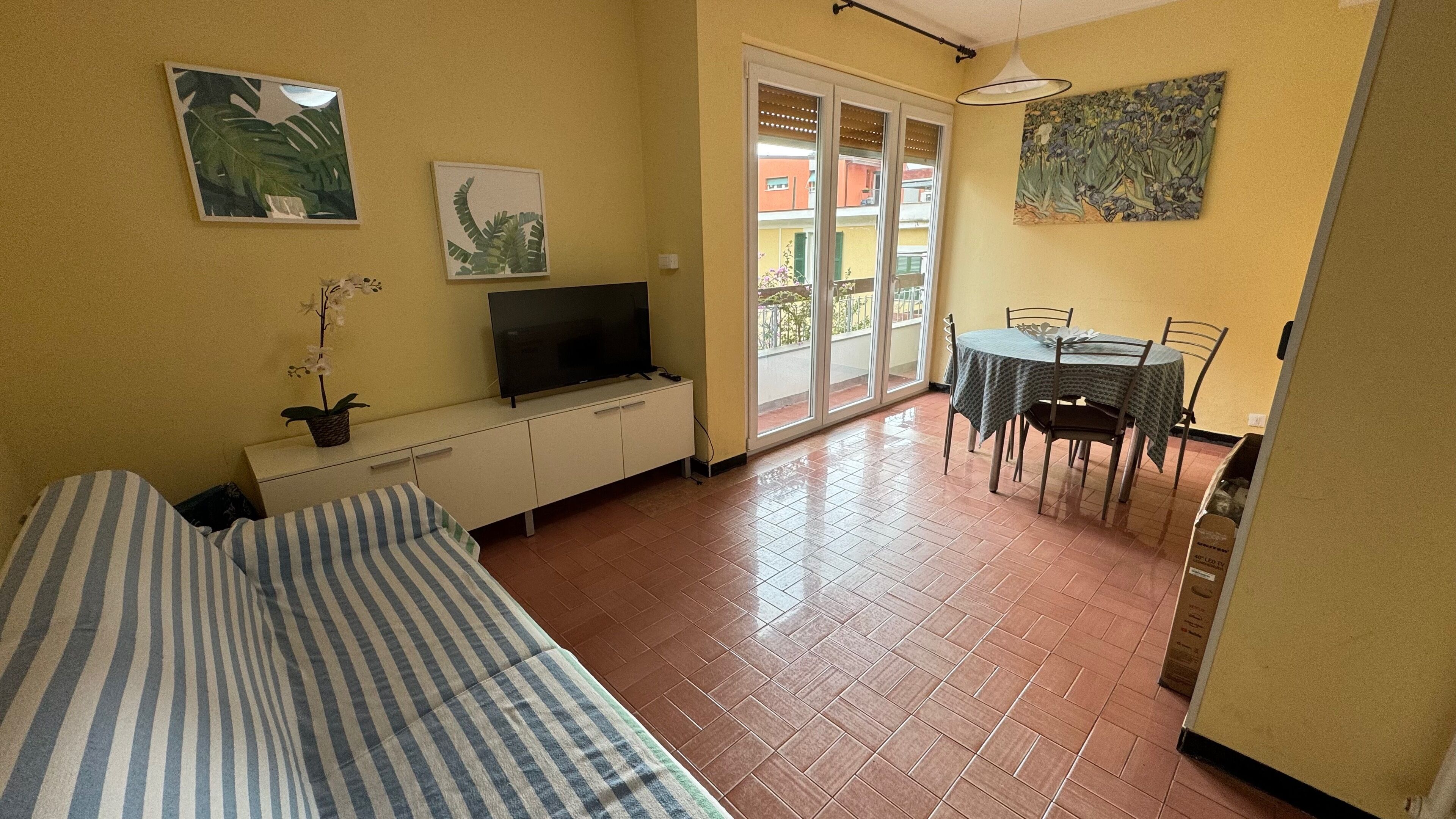 Une pièce comprenant un lit, un téléviseur posé sur un meuble, une table à manger avec des chaises et une porte-fenêtre coulissante donnant sur un espace extérieur.