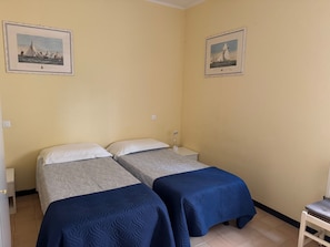 Une chambre avec deux lits, une table de chevet, une lampe et deux tableaux encadrés accrochés aux murs.