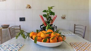 Una mesa de comedor con un cuenco de naranjas y una planta, rodeada de sillas y un mantel decorado.
