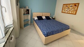 Une chambre à coucher avec un lit, une armoire, une étagère remplie de livres et une lampe fixée au mur.