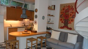 Cocina compacta con una isla central, taburetes de madera, un sofá gris y suelo a cuadros.