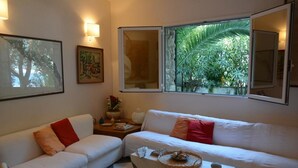 Un salón acogedor con un sofá blanco, una mesita con un mantel individual y una ventana con vistas a zonas verdes.