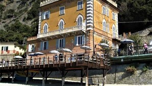 Ein mehrstöckiges Gebäude mit Balkonen, einer Terrasse mit Sitzgelegenheiten und einer Hanglage im Hintergrund.