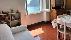 Ein Zimmer mit Meerblick, einem Esstisch mit Stühlen, einem Sofa, einem Schrank und einem Bücherregal.