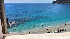 Ein Strand mit klarem türkisblauem Wasser, Menschen beim Schwimmen und Sonnenbaden, und Boote in der Ferne.