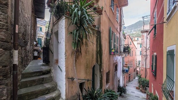 A narrow street with stone steps leading to a building with balconies and potted plants.