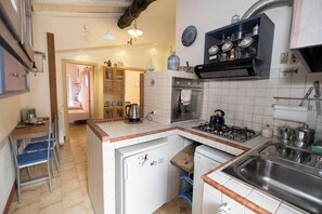 A compact kitchen with a gas stove, oven, and a sink. There is a small refrigerator and a cabinet with jars and containers.