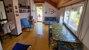Ein gemütliches Zimmer mit Holzbalkendecke, einem Esstisch mit Zitronenmuster, einem blauen Sofa und einem Sessel.