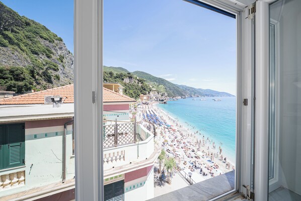 Une vue sur la côte depuis un balcon donnant sur une plage où l’on aperçoit des personnes et des bateaux.
