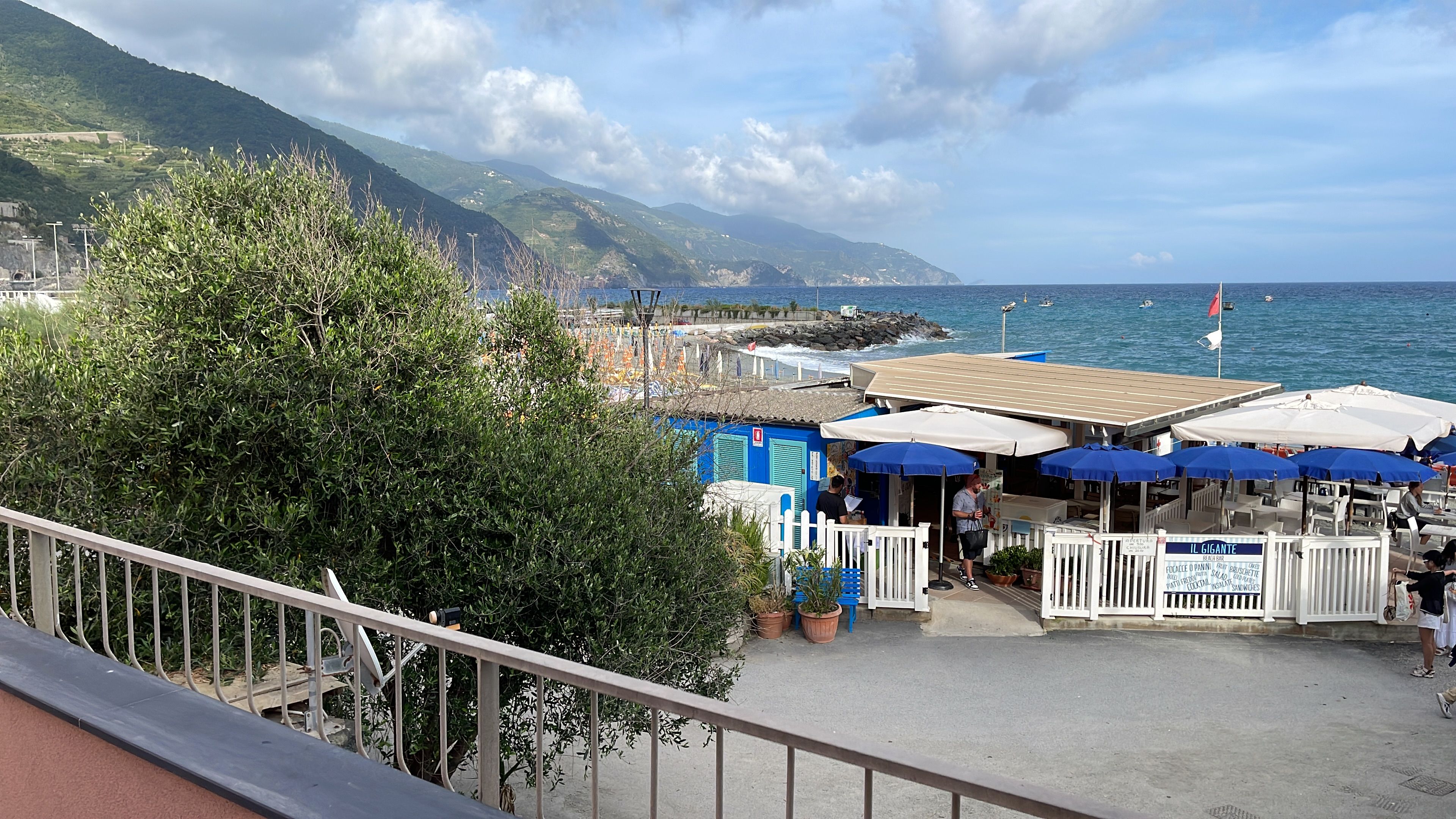 A coastal view with a restaurant patio, a white fence, and a mountain in the background.