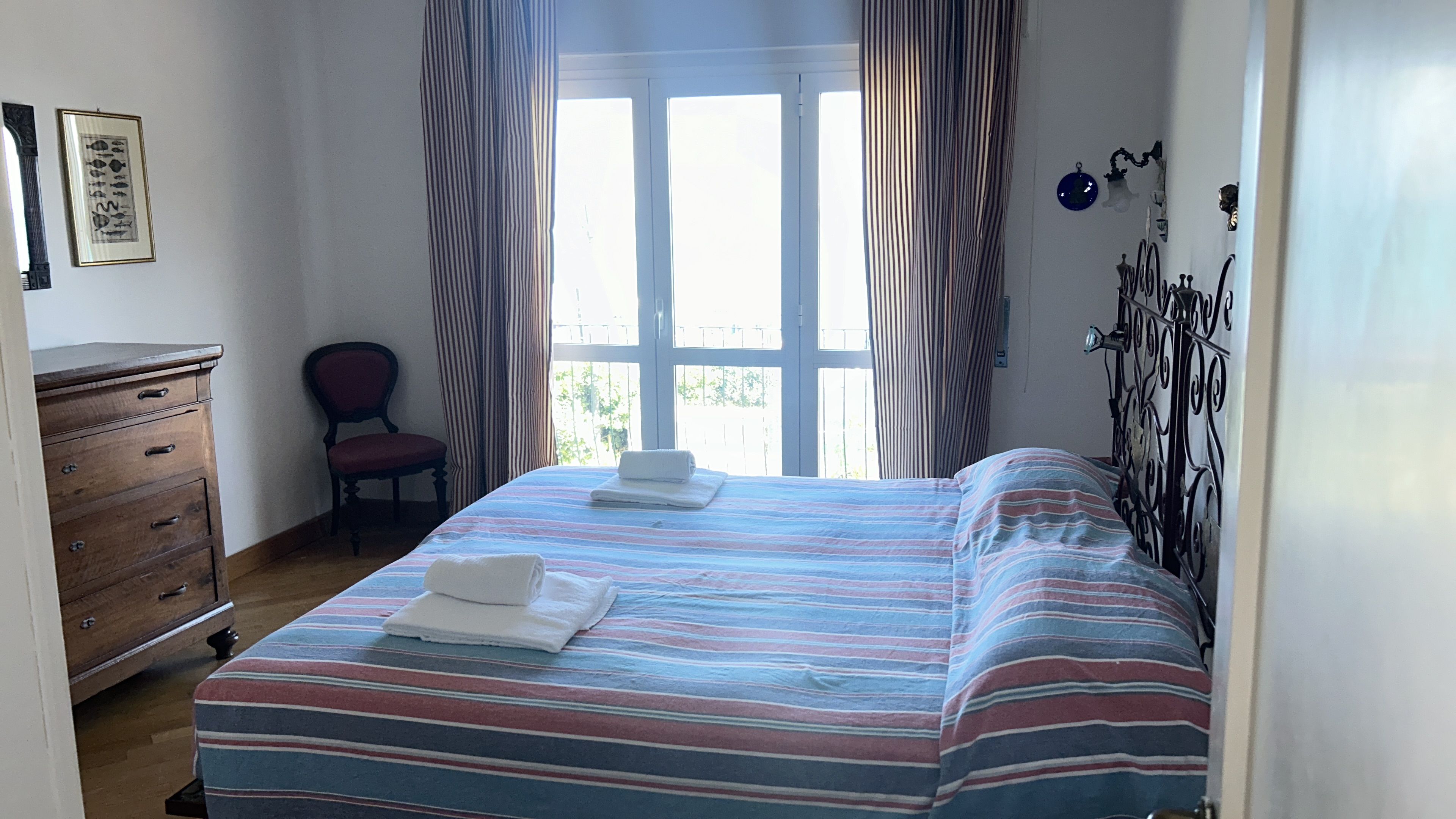 A bedroom with a bed, a chair, a dresser, and a window with curtains.