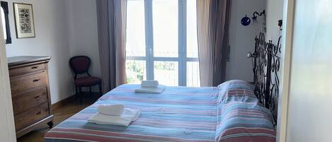A bedroom with a bed, a chair, a dresser, and a window with curtains.