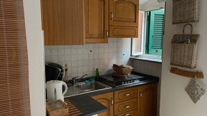 A compact kitchen with wooden cabinets, a black countertop, and a window with green shutters. - Dume Cosy Apt - Central - Near the beach with A.C. (Monterosso al Mare)