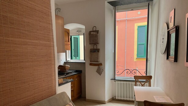 A compact living space with a kitchenette, a dining area, and a window with a view of a colorful building. - Dume Cosy Apt - Central - Near the beach with A.C. (Monterosso al Mare)
