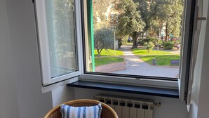 A corner room with a wicker chair and a view of a green park and hills.