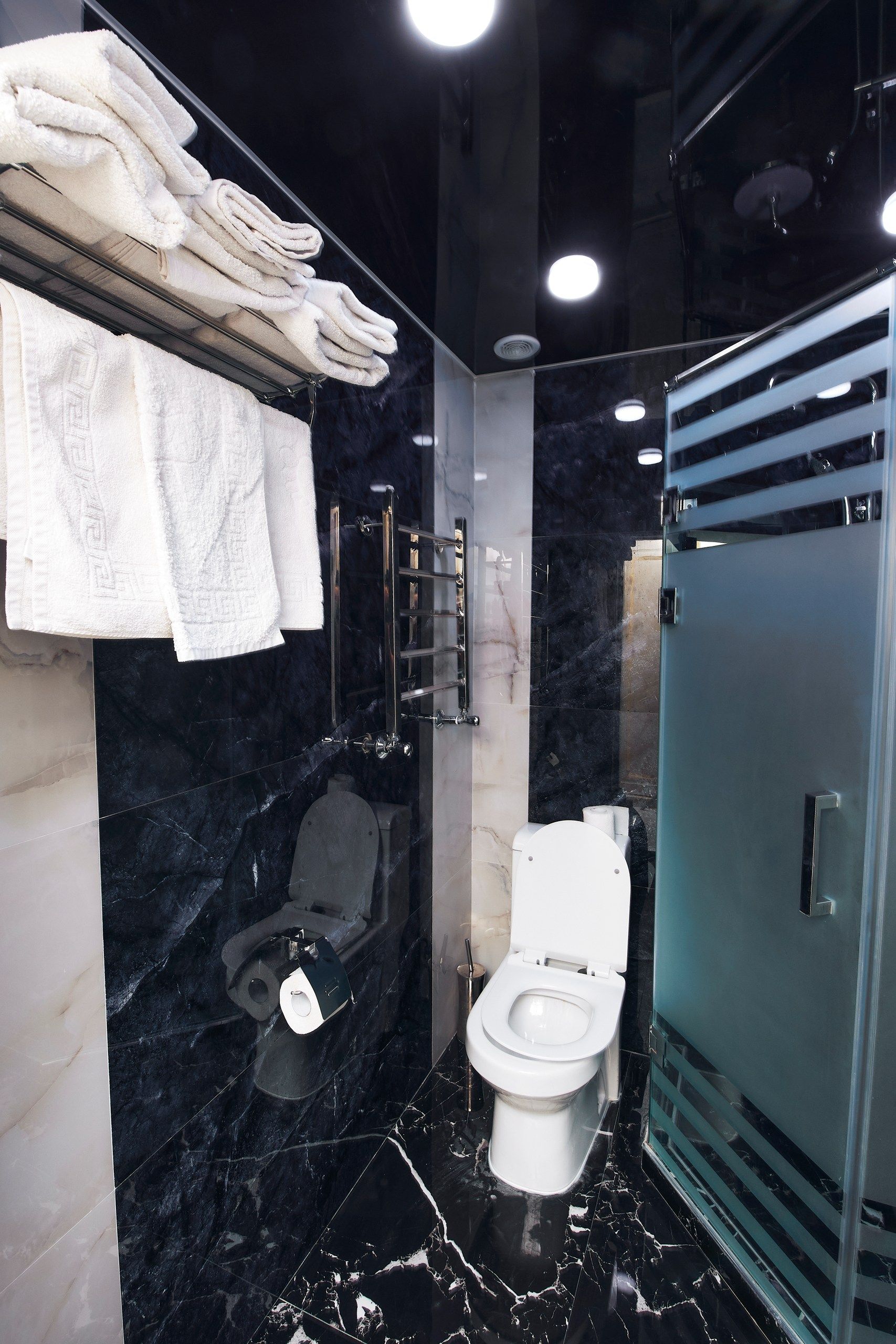 Un baño moderno con suelo de mármol, cabina de ducha de vidrio, inodoro y toallero con toallas dobladas.