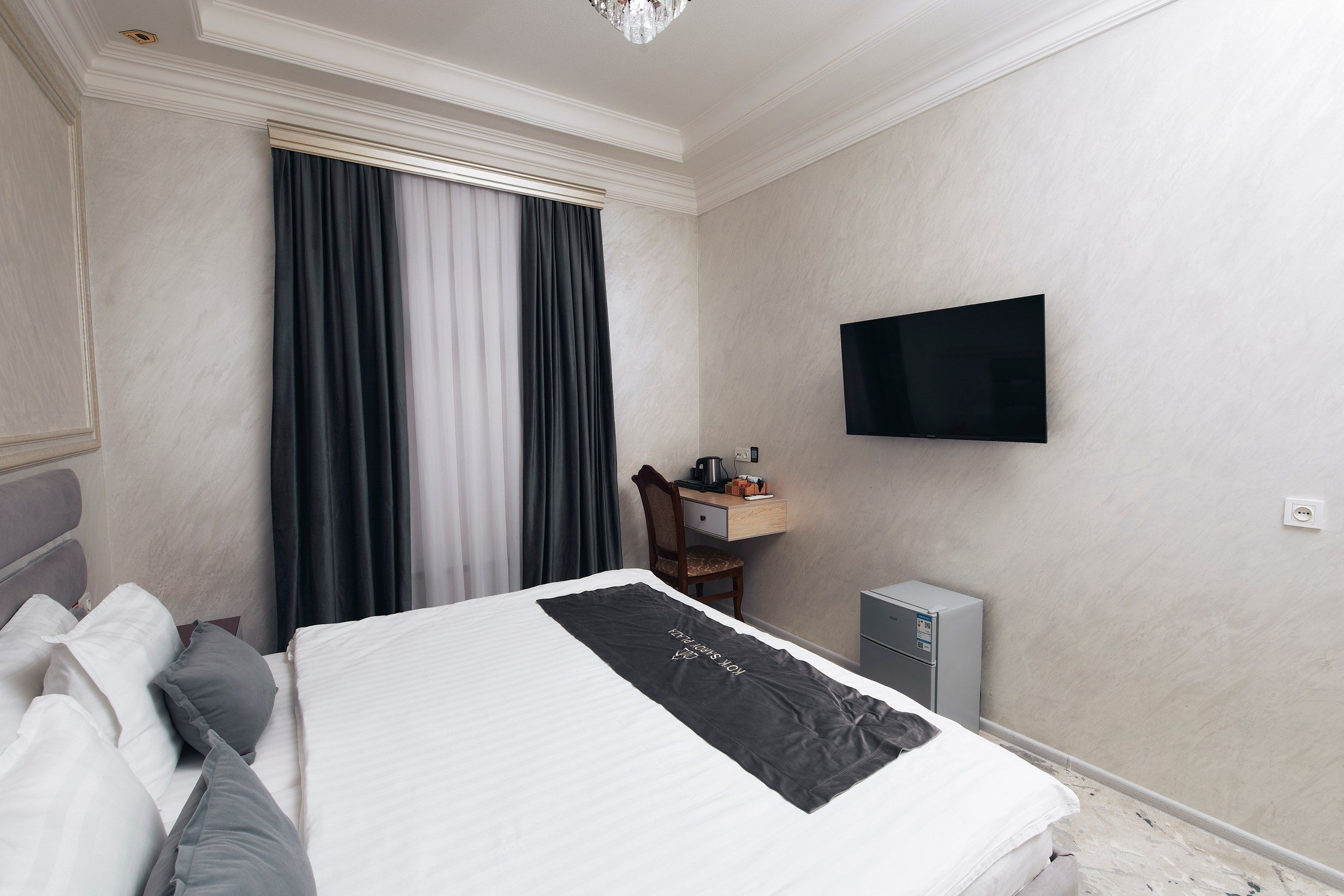 A hotel room with a bed, a desk, a chair, a television, and a small kitchenette.