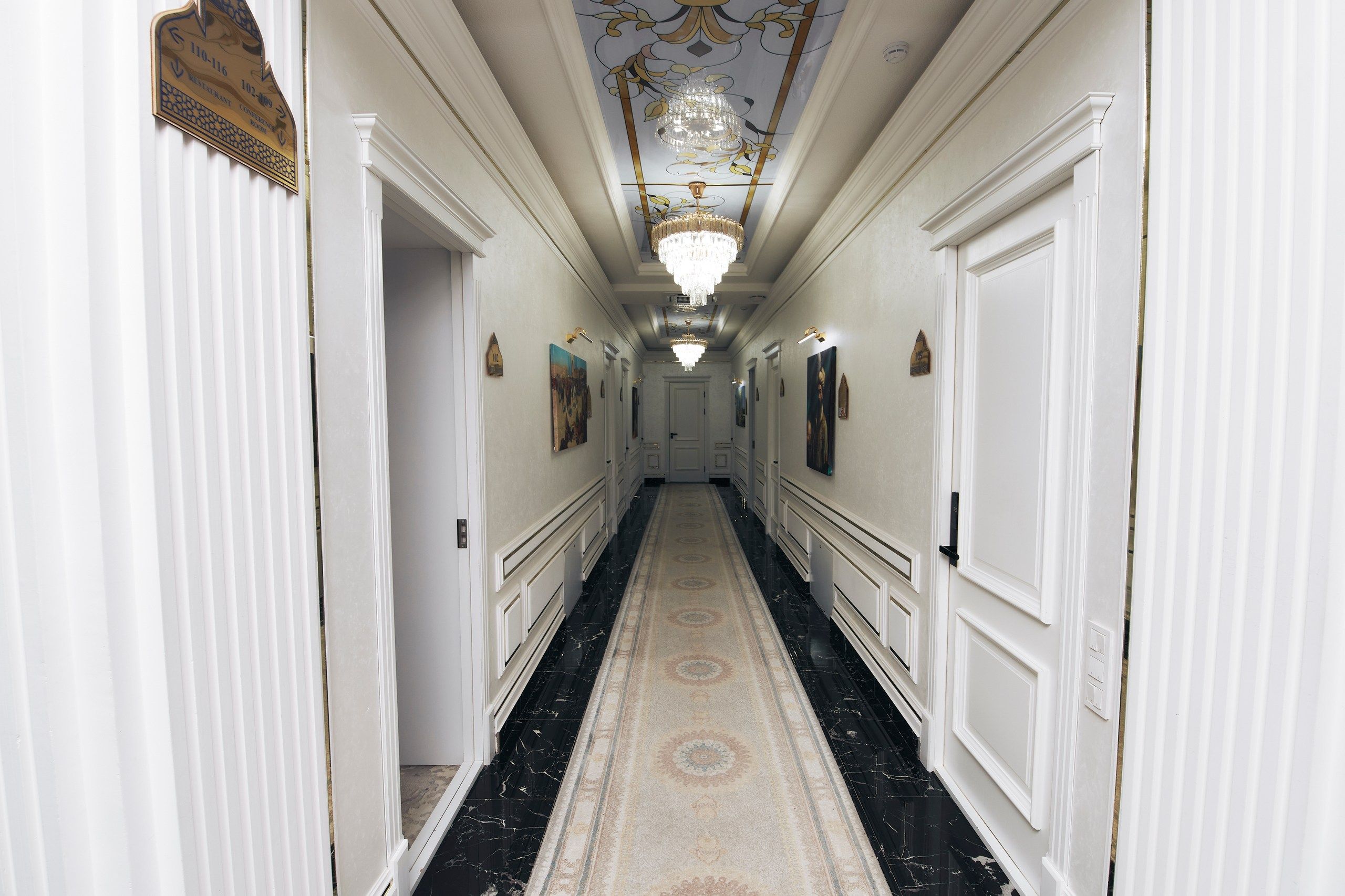 Un pasillo de hotel con piso de mármol, paredes blancas y un candelabro.