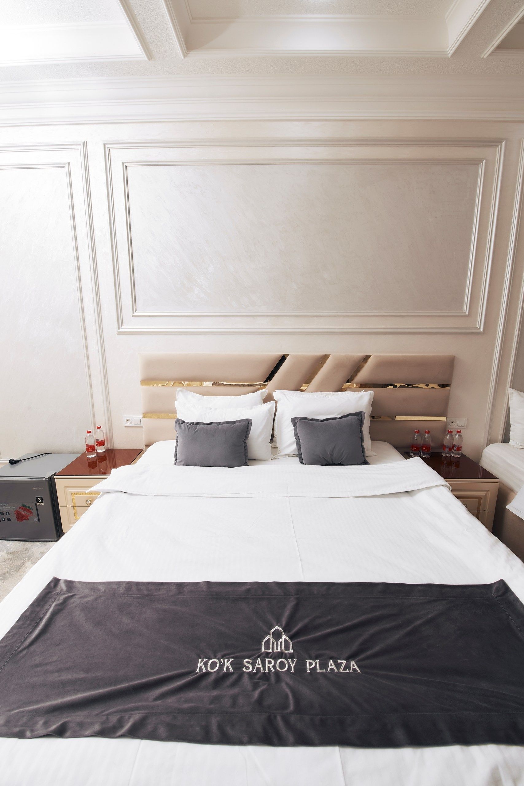 A hotel room with a large bed, a wooden headboard, and a minibar.