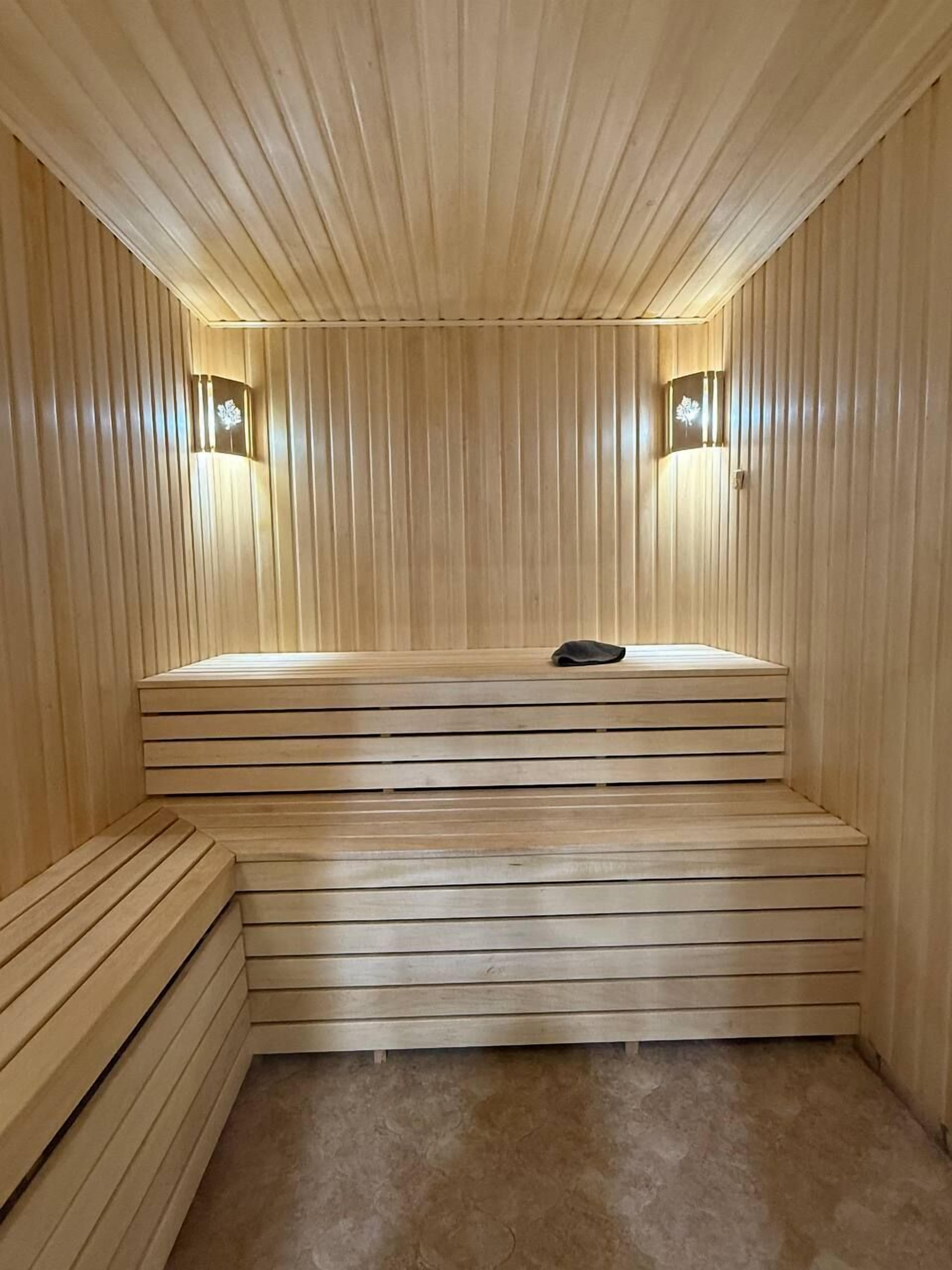 A sauna with wooden benches and slatted walls, featuring two wall-mounted light fixtures.