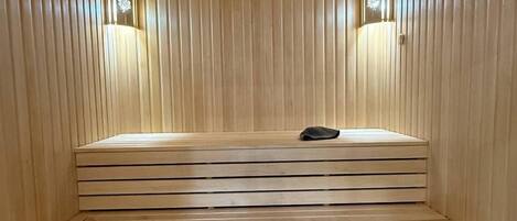 A sauna with wooden benches and slatted walls, featuring two wall-mounted light fixtures.