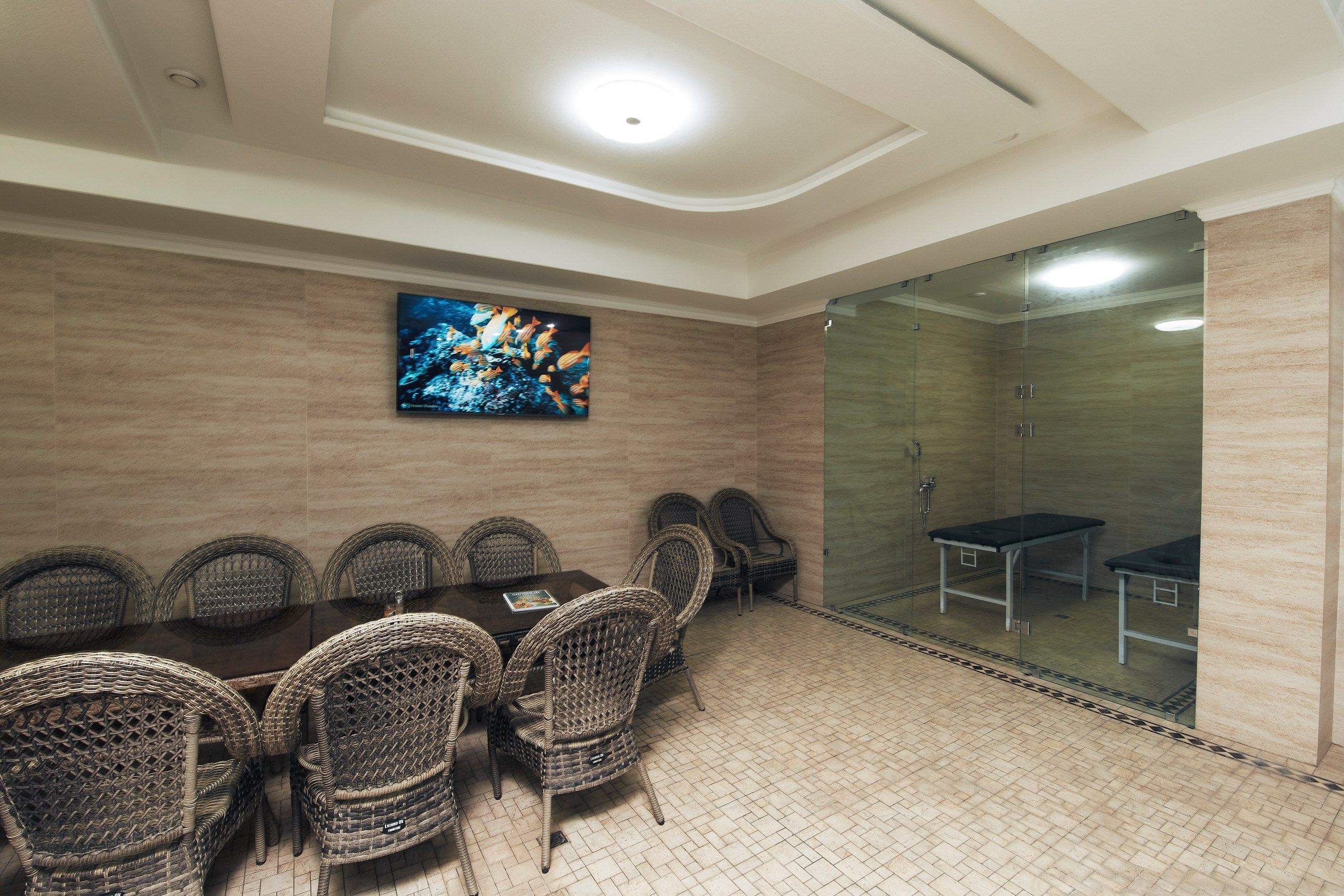 A conference room with a long table, wicker chairs, a television screen, and a glass partition.
