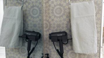 A bathroom with two hair dryers mounted on the wall, a towel rack with two white towels, and a patterned tile backsplash.