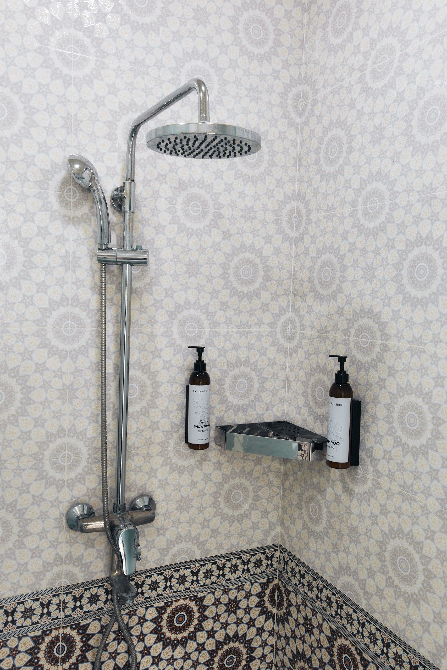 A shower with a handheld showerhead and a wall-mounted faucet. There are two bottles of shampoo and conditioner on a shelf.