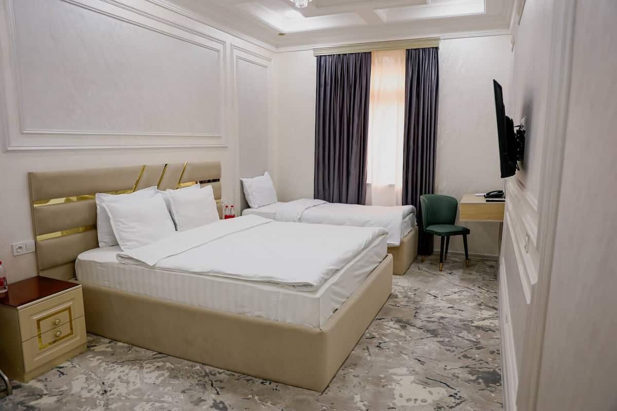 A hotel room with two beds, a desk, a chair, and a television.