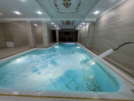 A swimming pool with a water fountain feature, surrounded by tiled walls and a decorative ceiling.