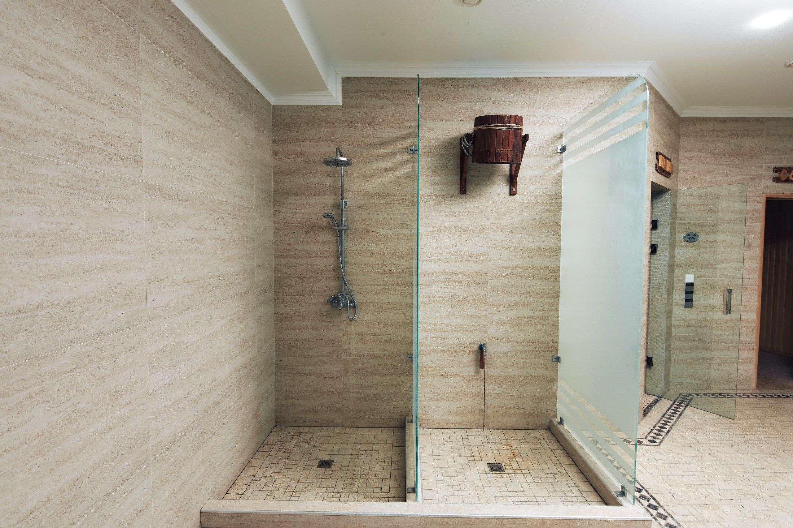A walk-in shower with a glass door, a wooden bucket, and a tiled floor.