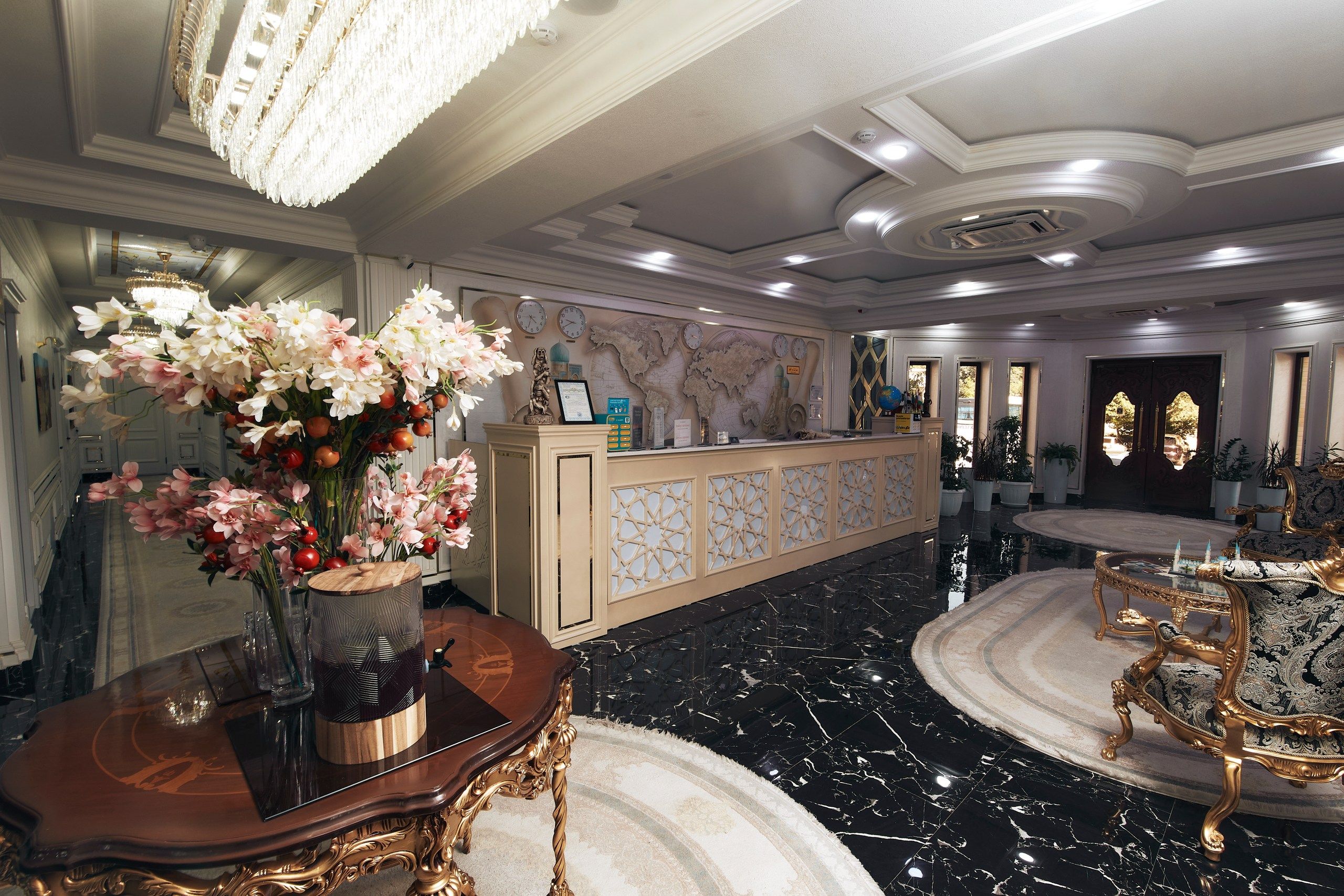 A lobby with a reception desk, a chandelier, a vase of flowers, and a marble floor.