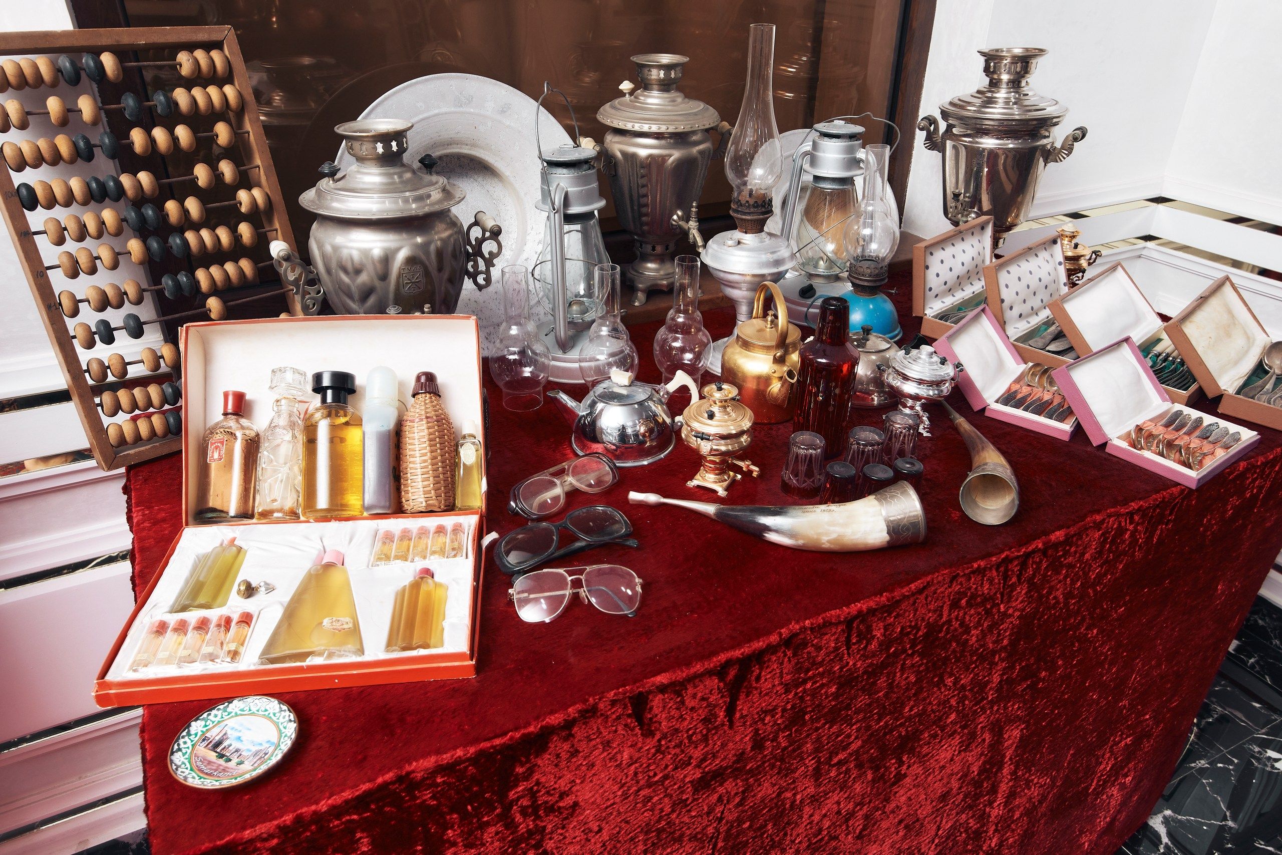 Une collection d’objets anciens comprenant un boulier en bois, divers articles en verre et des récipients en métal, le tout disposé sur une table recouverte de velours rouge.