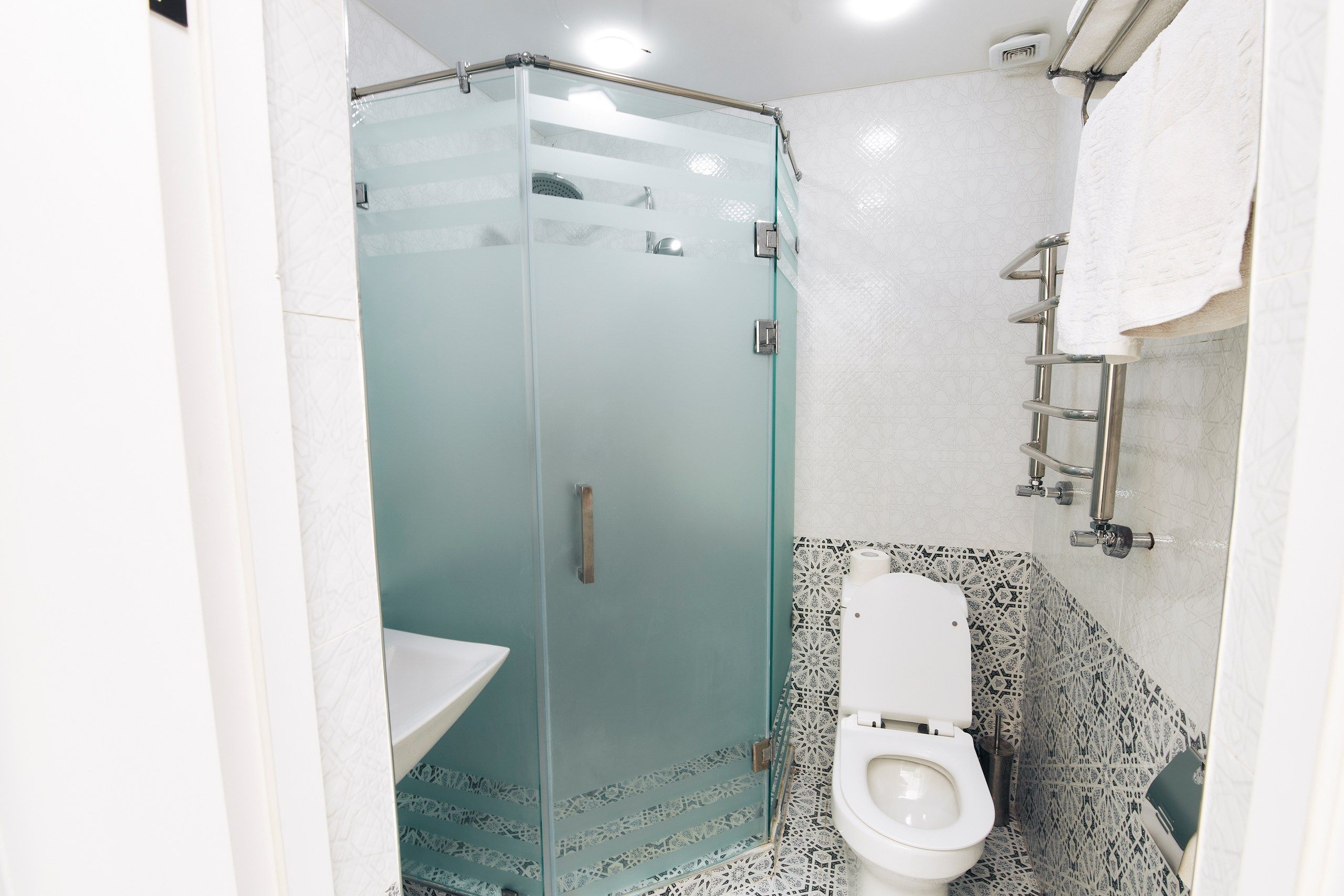 Un baño moderno con ducha de vidrio, inodoro blanco y azulejos estampados.