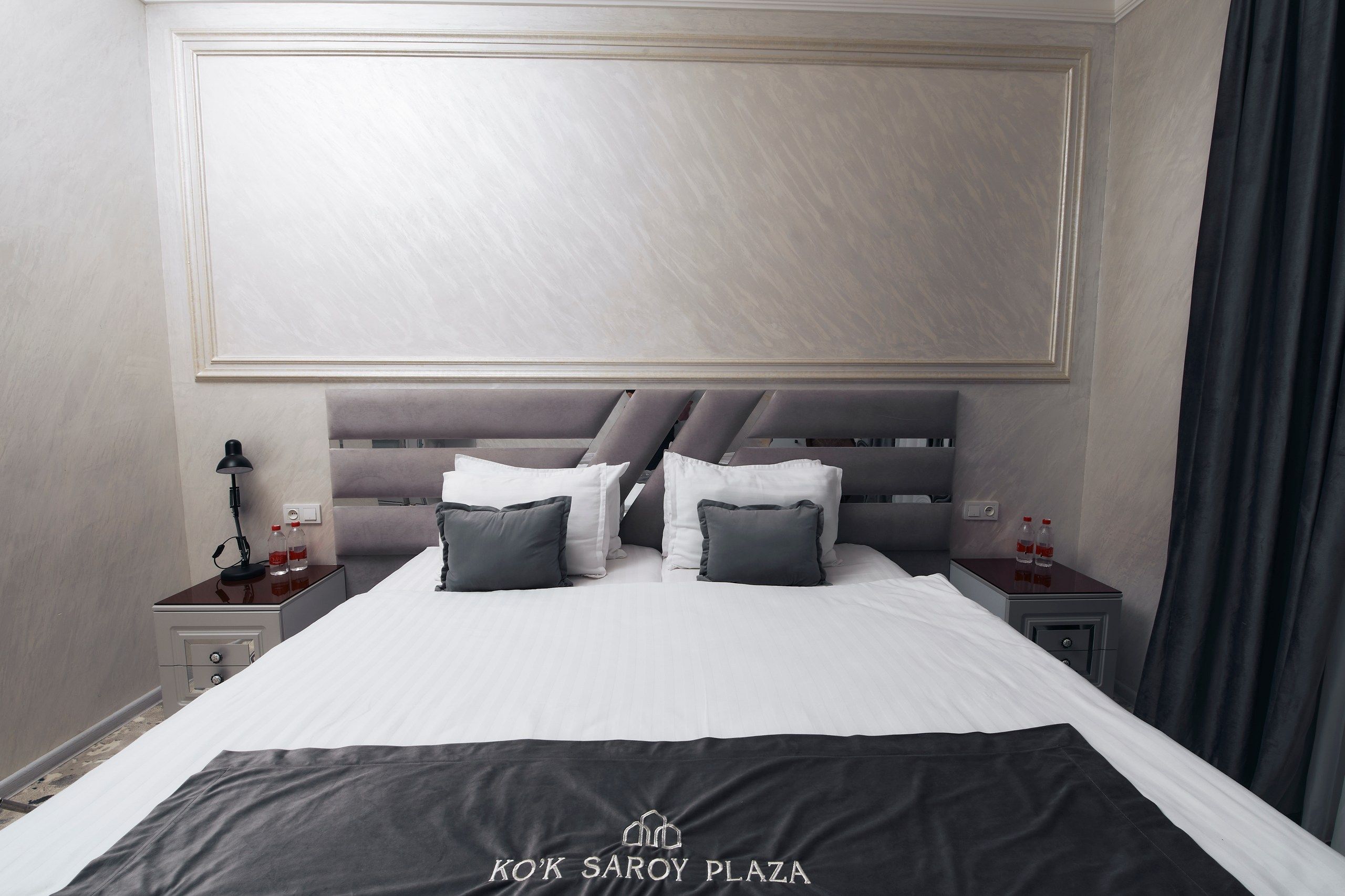 A hotel room with a large bed, a headboard, two bedside tables, and a nightstand.