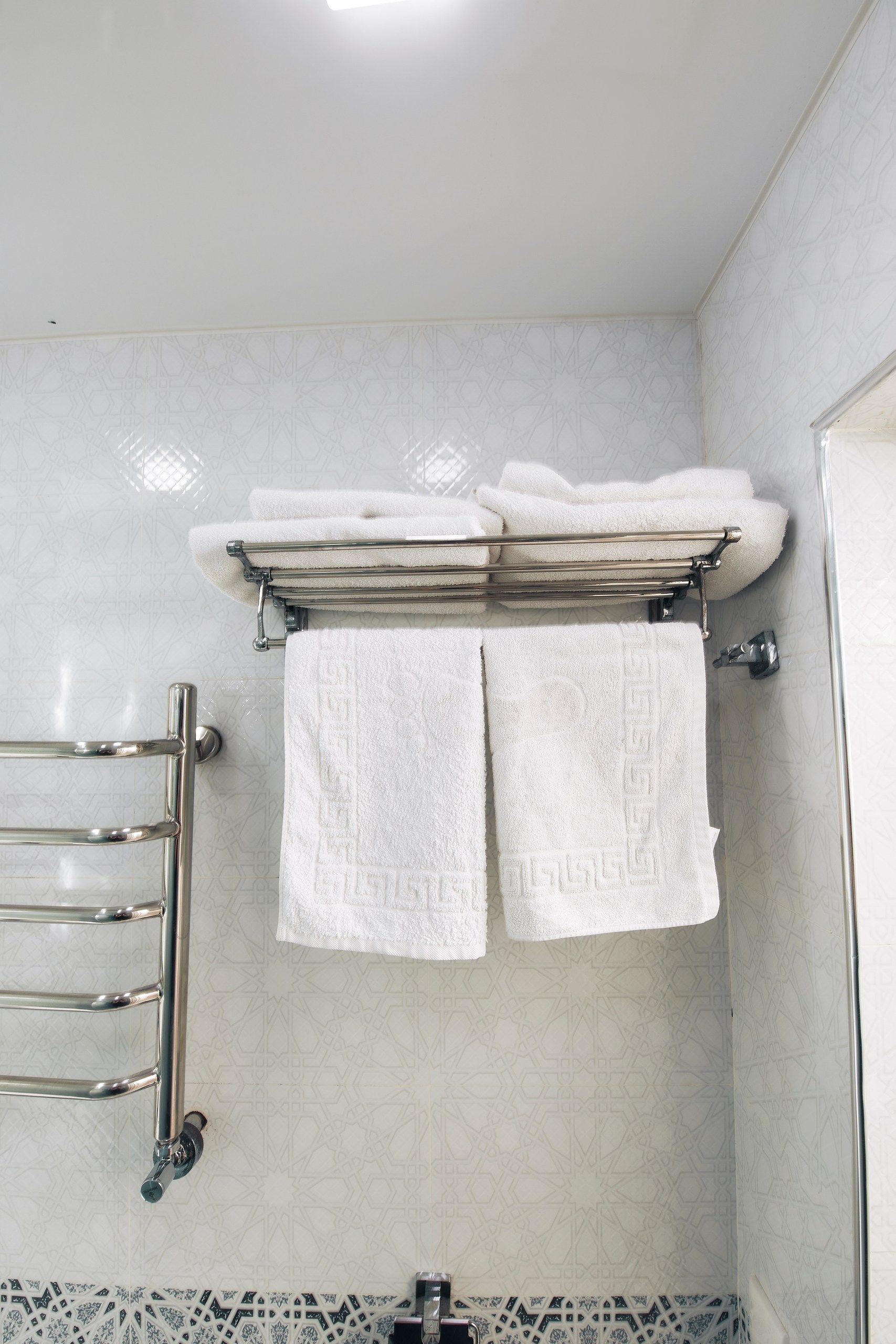 Une salle de bain équipée d’un porte-serviettes sur lequel sont posées deux serviettes, d’une zone de douche et d’un pare-feu en carreaux à motifs.