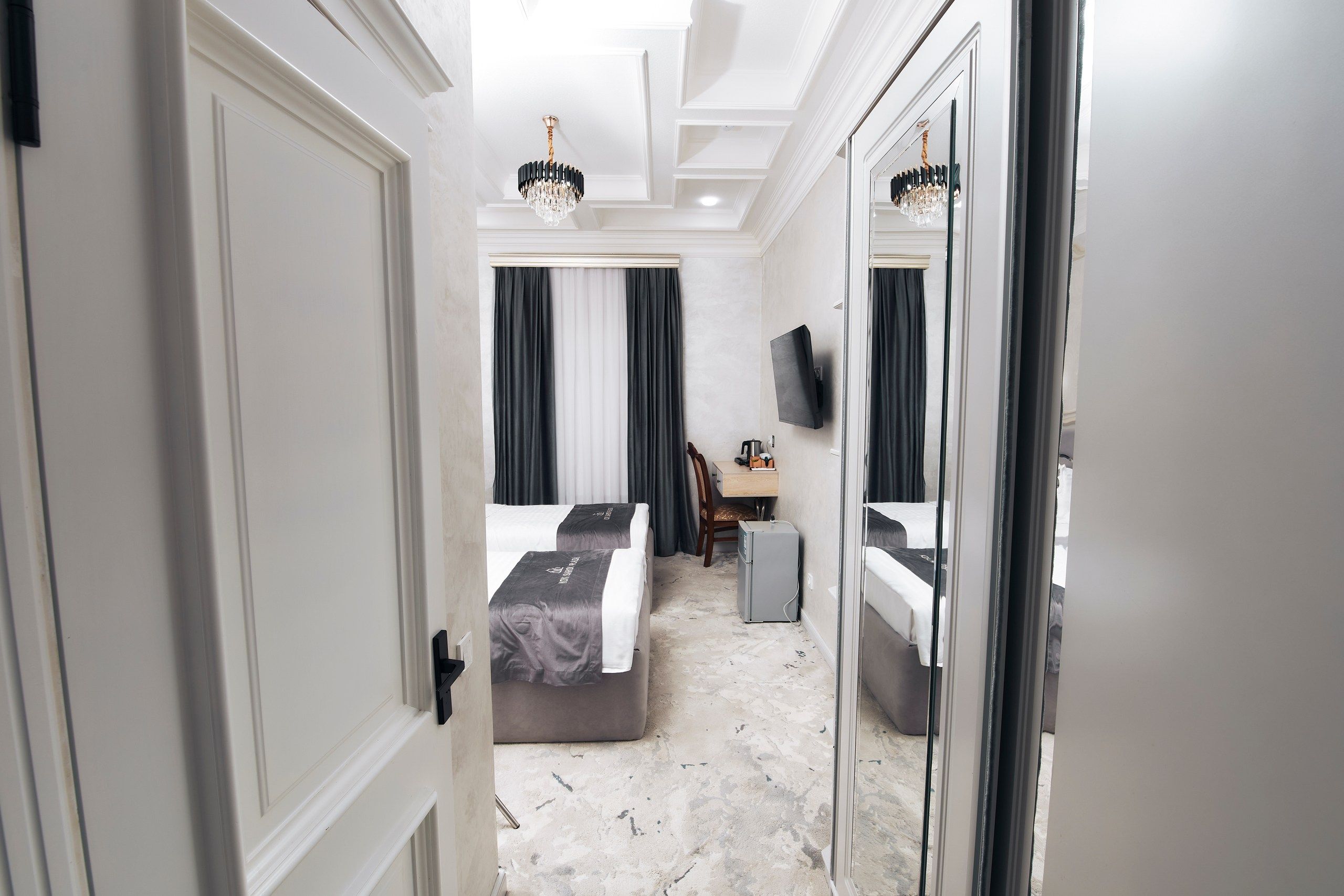 A hotel room with a bed, a desk, a chair, a television, and a mirror.