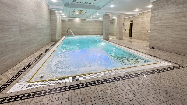 An indoor swimming pool with a tiled floor and walls, surrounded by a patterned border.