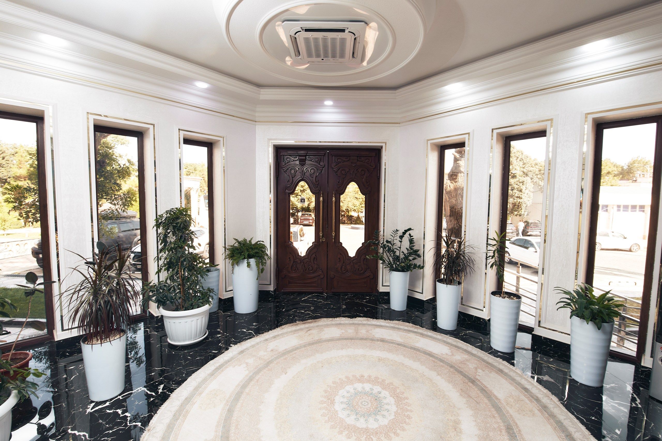 A lobby with a marble floor, a central rug, and potted plants.