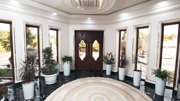A lobby with a marble floor, a central rug, and potted plants.