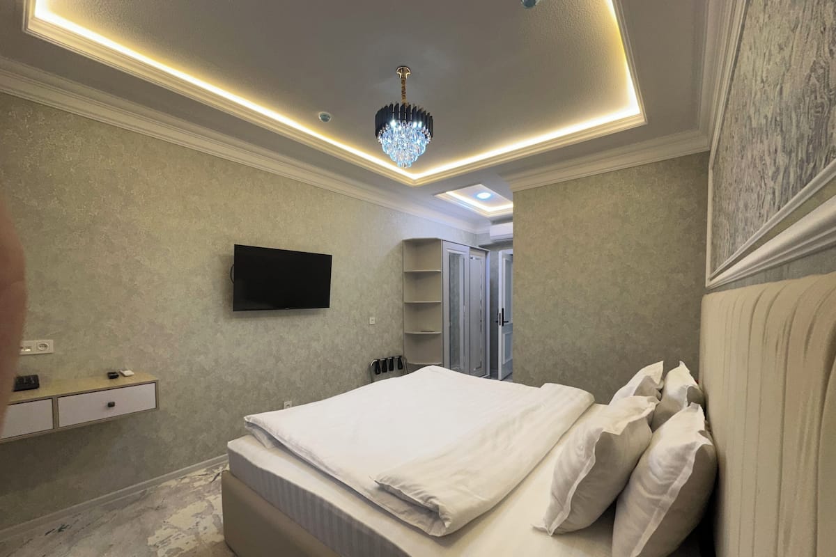 A bedroom with a bed, a TV, a chandelier, and a wardrobe.