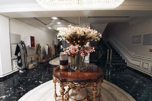Un pasillo con suelo de mármol, un gran candelabro, una consola decorativa con un florero y una escalera.