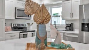 Une cuisine moderne avec des meubles blancs, des appareils en acier inoxydable et un îlot central agrémenté d’objets décoratifs.