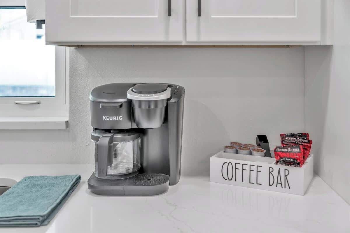 En Keurig-kaffemaskin står på en vit bänkskiva, och bredvid den finns en skylt med texten ”kafé” samt kaffekapslar.