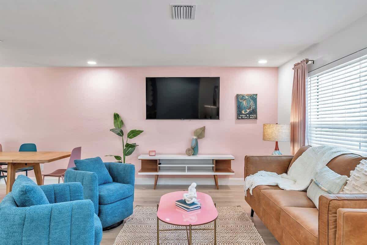 Una sala de estar con pared rosa, televisor de pantalla plana, sofá, mesa de centro y comedor.