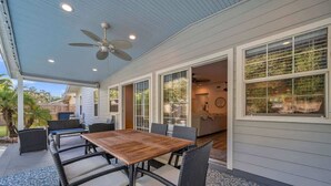 An outdoor patio with a wooden table and wicker chairs, a ceiling fan, and a view of the backyard. - Heated Pool, Stylish Home | Grand Cypress Retreat (Clearwater)
