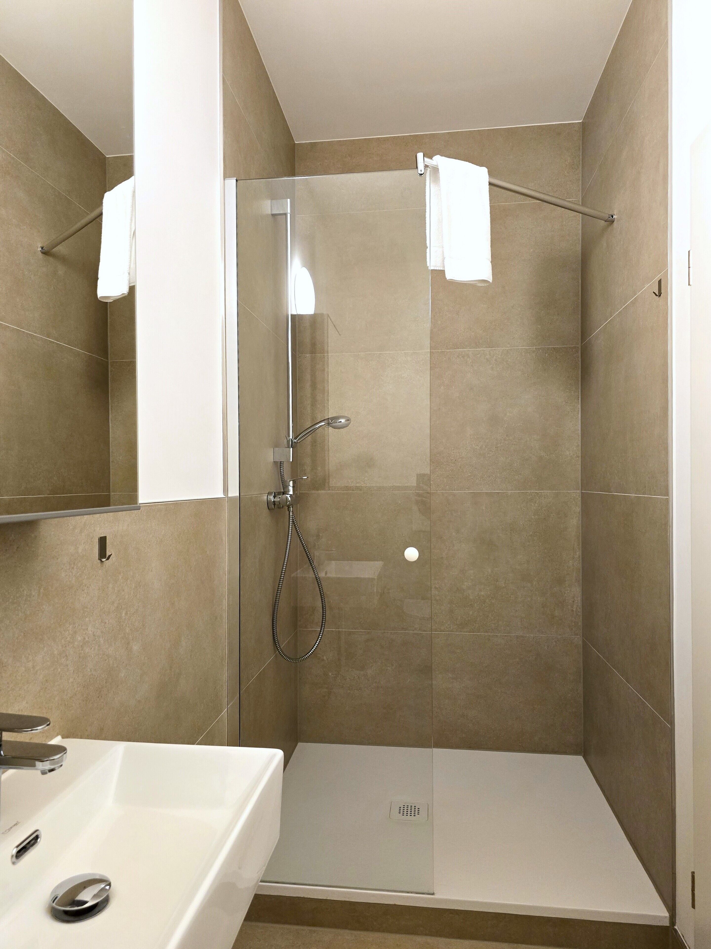 Une salle de bain moderne avec une douche à parois de verre, un lavabo blanc et un grand miroir.