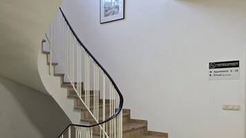A spiral staircase with white railings and beige steps, leading to a landing with a framed picture and a sign indicating private apartments 6-10.