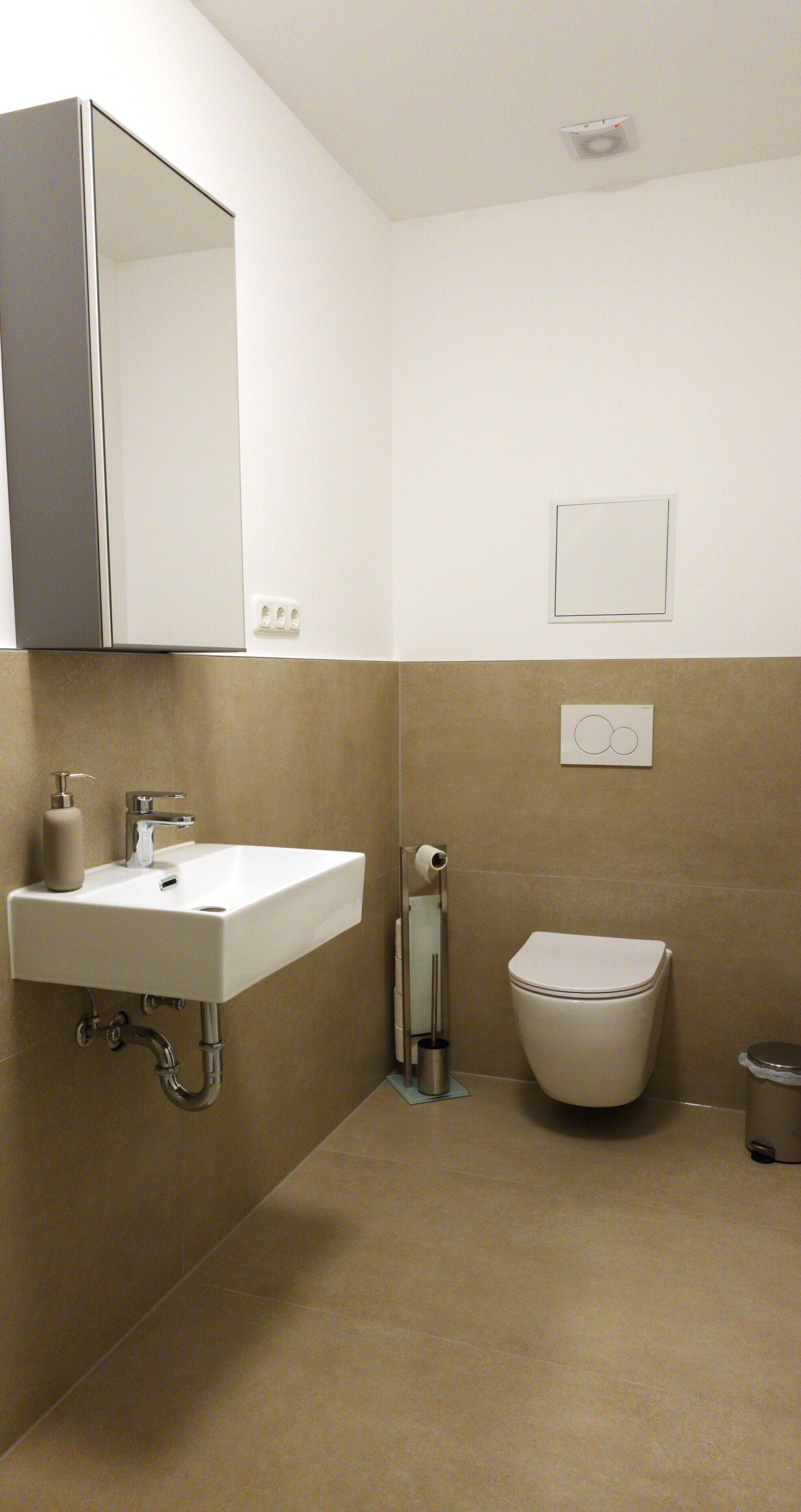 Une salle de bain équipée d’un lavabo, d’un miroir, de toilettes et d’une poubelle.