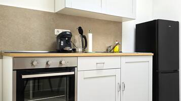 Eine kompakte Küche mit Backofen, Kaffeemaschine und einem schwarzen Kühlschrank.